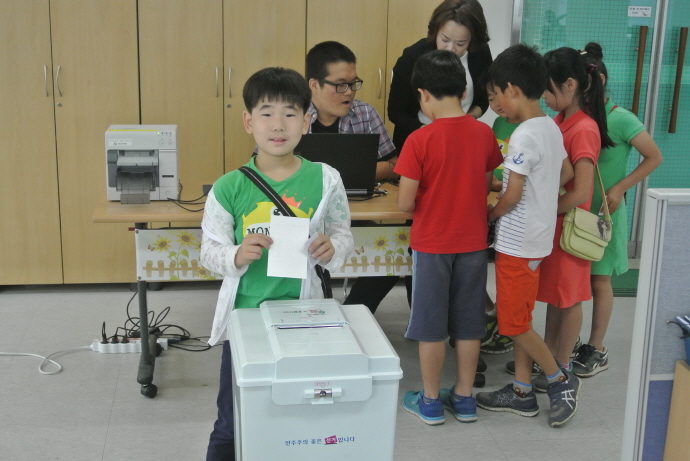 사전투표운용장비를 이용하여 학생들이 본인확인 후 투표함에 투표지를 투입하는 장면의 사진입니다.