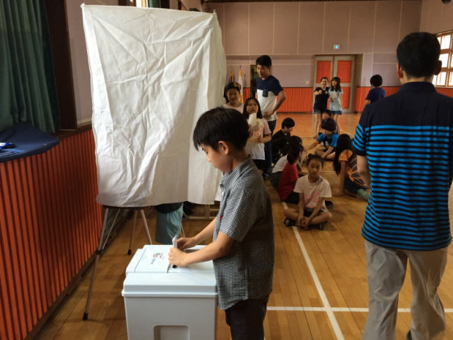 투표용지를 교부받아 기표소에서 기표한 후 투표함에 투표지를 투입하고 있는 모습의 사진입니다.
