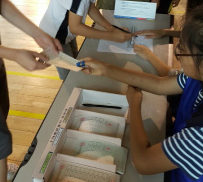 석성초등학교 학생들이 본인확인석에서 본인확인 후 3장의 투표용지를 수령하고 있는 모습의 사진입니다.