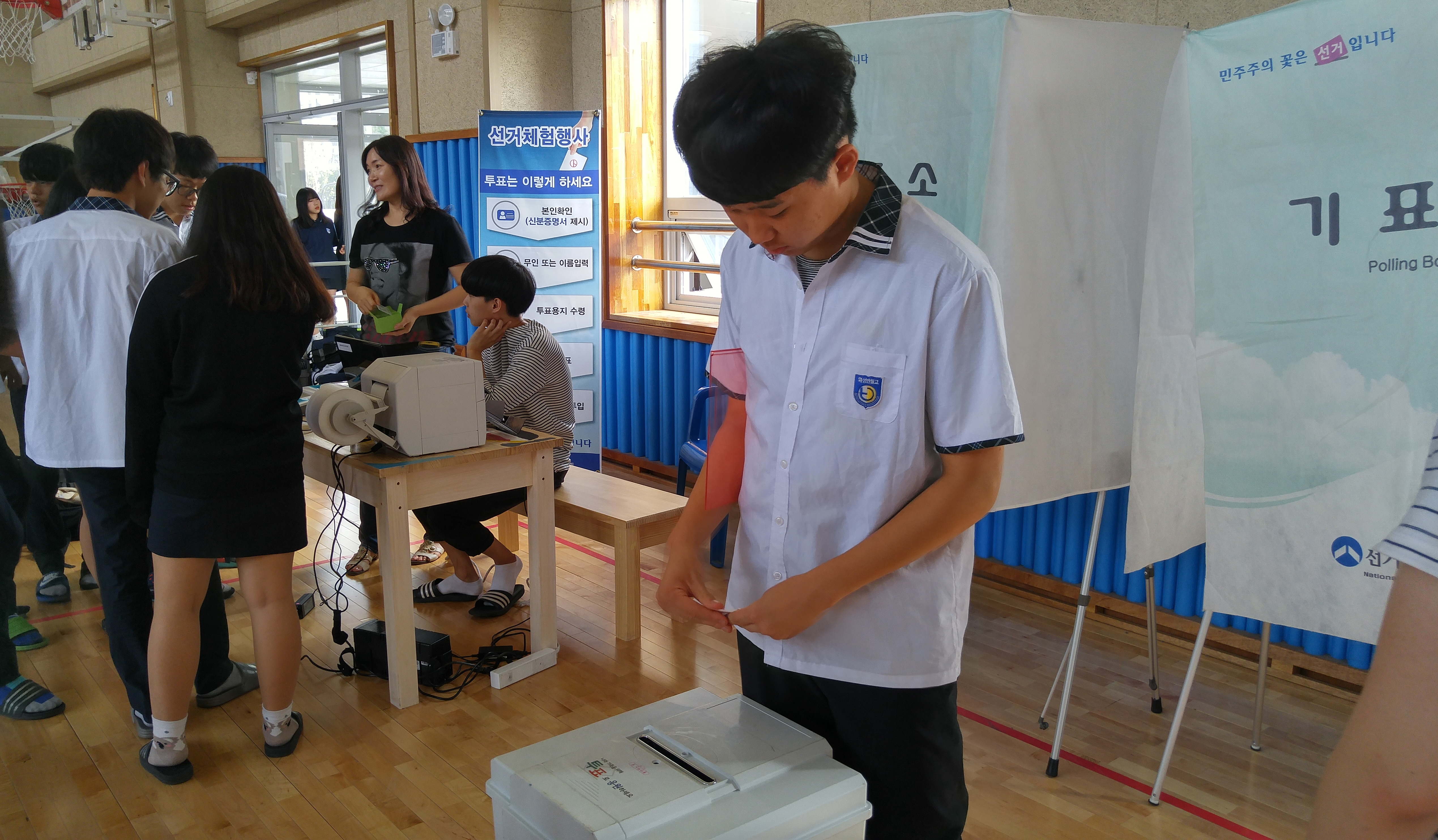 투표용지발급기를 이용한 선거체험행사에 학생들이 참여하고 있는 사진