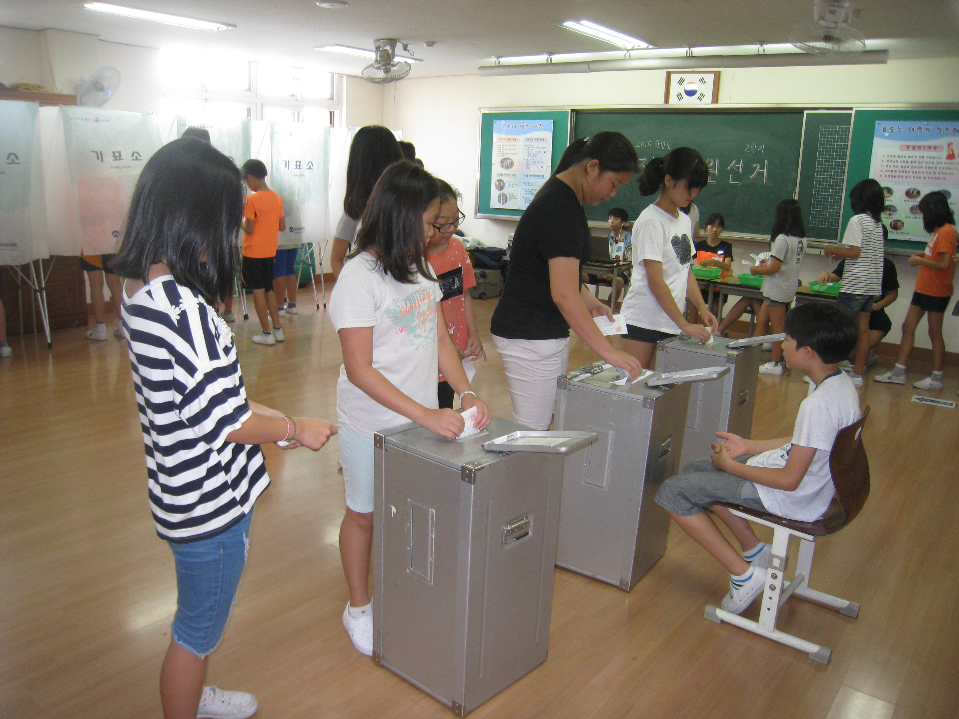 학생들이 기표소에서 기표후 투표함에 투표지를 투입하고 있는 모습의 사진입니다.