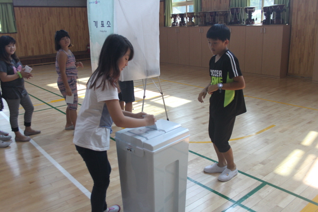 기표소에서 기표한 투표용지를 투표함에 투입하고 있는 어린이들의 모습입니다.