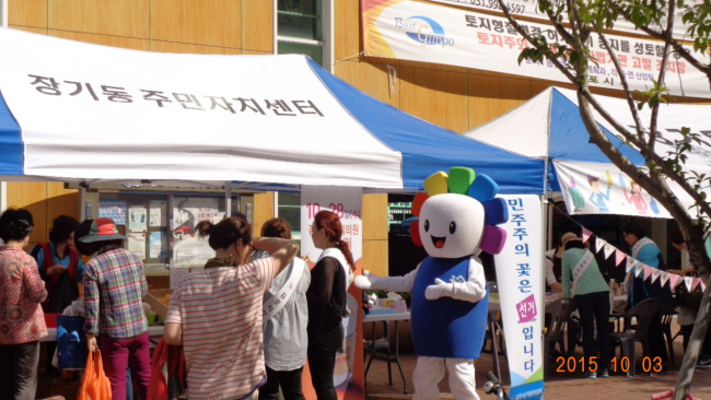 위원회 직원들이 X배너 및 캐릭터 탈인형을 활용하여 10. 28. 김포시의회의원재선거 투표참여 홍보활동 전개하고 있는 모습의 사진입니다.